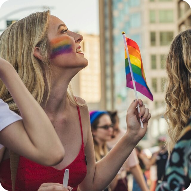 woman identifying pridefest with pride flag facepainting and holding a pride flag
